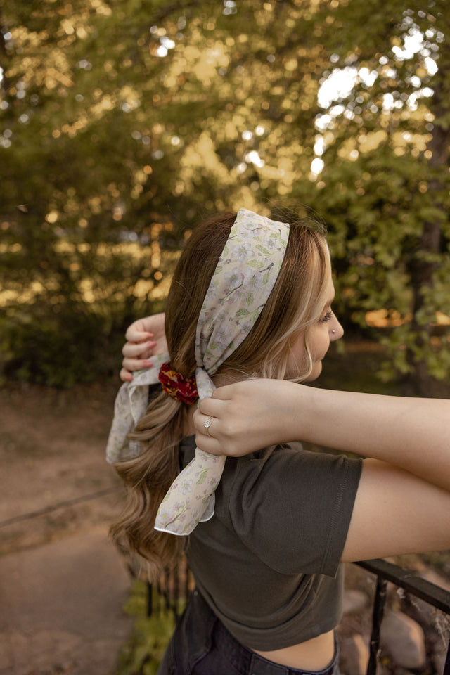Apple Blossom State Flower Scarf. A apple blossom scarf with a yellow background is being tied up into a young woman's hair.