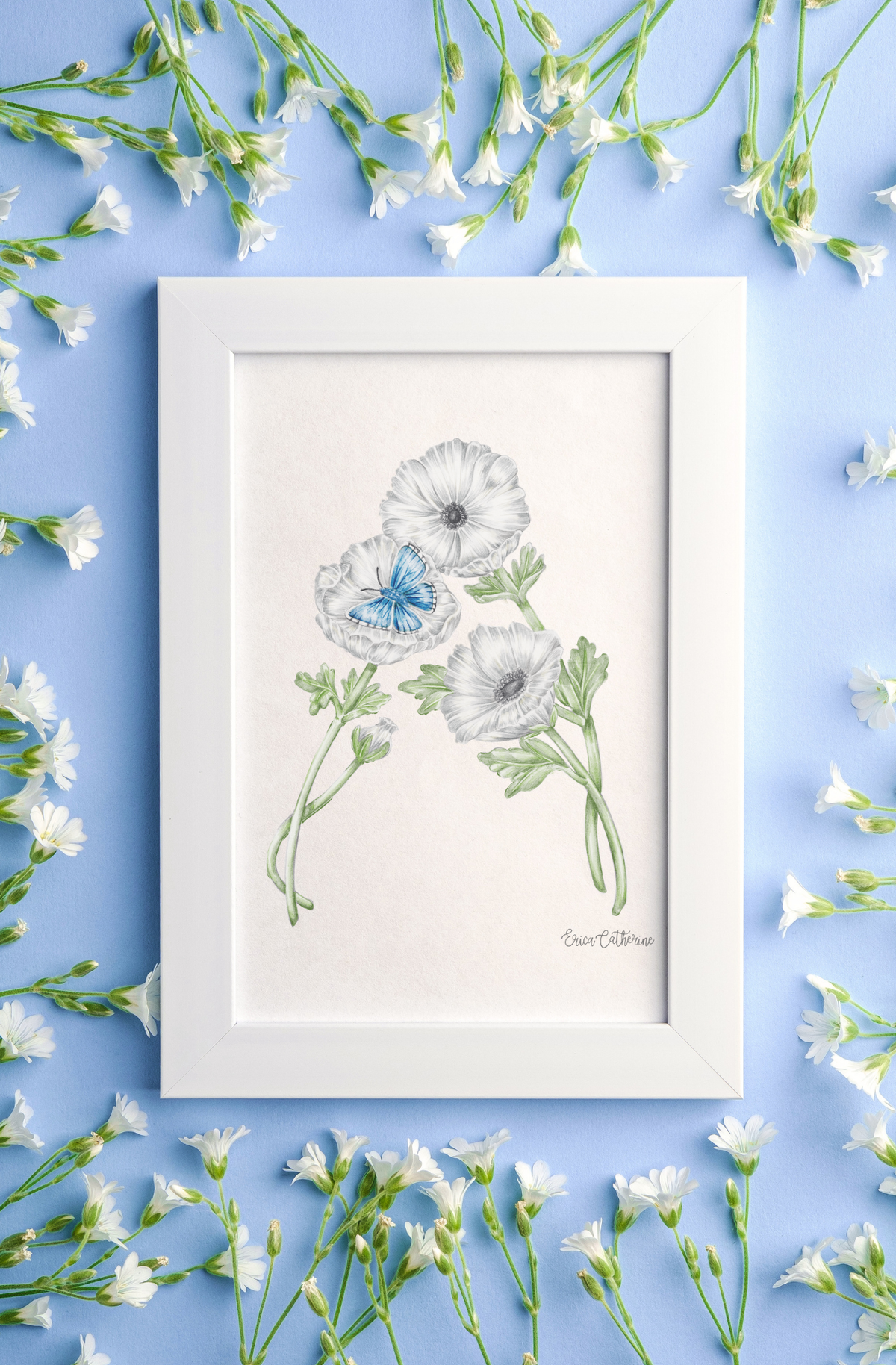 A framed botanical art print "A" featuring three white flowers with one blue butterfly displayed on a light blue background with scattered white flowers.