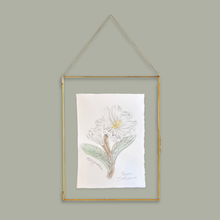 Load image into Gallery viewer, A framed botanical art print featuring a white flower with green leaves, hanging from a gold metal frame and chain against a solid sage green background.