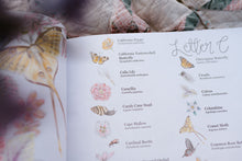 Load image into Gallery viewer, Open book with illustrations of butterflies and flowers on a floral fabric background