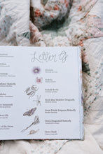 Load image into Gallery viewer, Open book with letter 'G' and illustrations on a floral fabric background