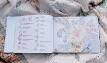 Load image into Gallery viewer, Open book with illustrations of flowers and text on a floral fabric background