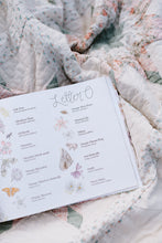 Load image into Gallery viewer, Open book of floral illustrations and text on a floral blanket