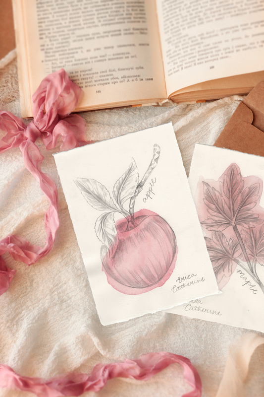 Two artworks featuring botanical illustrations of apples and maple leaves, styled on a beige fabric with a pink ribbon and an open book in the background.