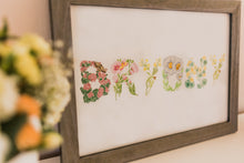 Load image into Gallery viewer, A framed floral art print featuring the word 'Bryony' spelled out with embroidered flowers and leaves on a white background, housed in a rustic gray-brown wooden frame.
