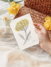 Load image into Gallery viewer, A hand holds a small piece of artwork featuring a yellow Milkweed flower illustration, styled on soft cream fabric with yellow flowers and a woven brown mat in the background.
