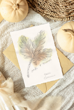 Load image into Gallery viewer, A flat-lay of an artwork featuring a watercolor oak leaf and acorn illustration with the text 'oak + acorn' and Erica Catherine's Signature. The artwork is styled on a textured neutral fabric with kraft paper envelopes, autumn pumpkins, and a woven basket.
