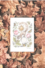Load image into Gallery viewer, A white art print featuring a whimsical autumn illustration of a squirrel, sun, butterflies, and flowers, laid flat on a bed of brown and copper-colored fallen leaves. The artist's signature is visible in the bottom right corner of the print.
