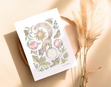 Load image into Gallery viewer, A white art print featuring a whimsical watercolor illustration of a gray squirrel plants, green leaves, moon and a sun, styled on a beige surface next to dried pampas grass.
